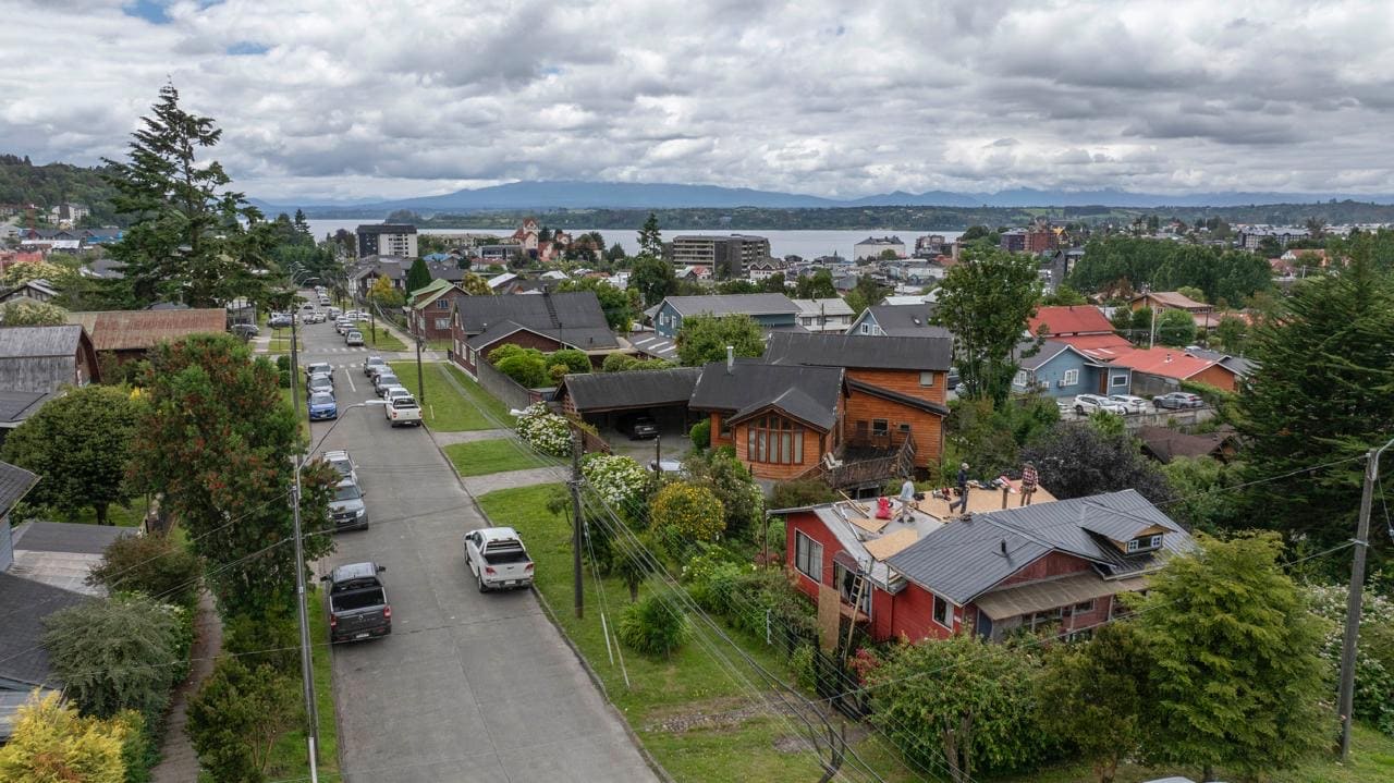 Vista aérea de Puerto Varas con el lago Llanquihue de fondo, mientras el equipo de Alero Construcciones trabaja sobre la techumbre de una casa de madera