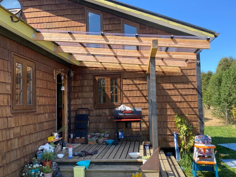 Pérgola de vigas de madera con cubierta de policarbonato sobre una terraza con deck